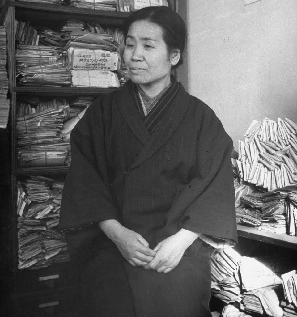 Portrait photograph of Tsuneko Okazaki, the scientist after whom Okazaki fragments are named, seated among laboratory notebooks