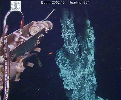 Underwater photograph of a remotely operated vehicle's arm sampling fluid beside a hydrothermal vent chimney, unlabelled
